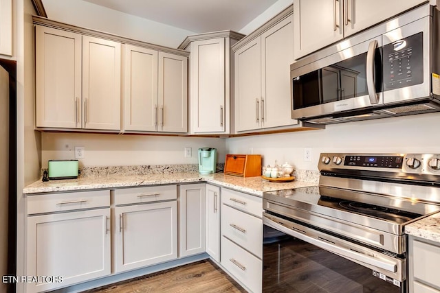 kitchen featuring light wood-type flooring, stainless steel appliances, and light stone counters