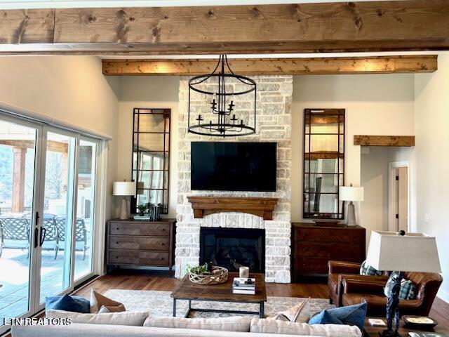 living room with beam ceiling, a stone fireplace, a chandelier, and wood finished floors