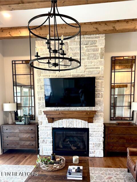 living area with beam ceiling, a fireplace, an inviting chandelier, and wood finished floors