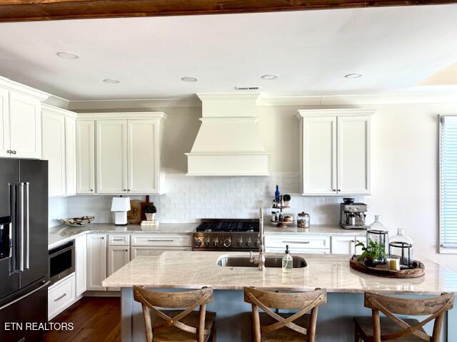 kitchen with range with gas stovetop, custom range hood, light stone counters, and high end fridge