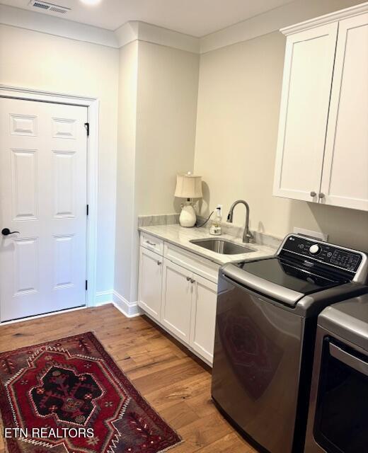 laundry room featuring cabinet space, ornamental molding, a sink, light wood-style floors, and washer and dryer