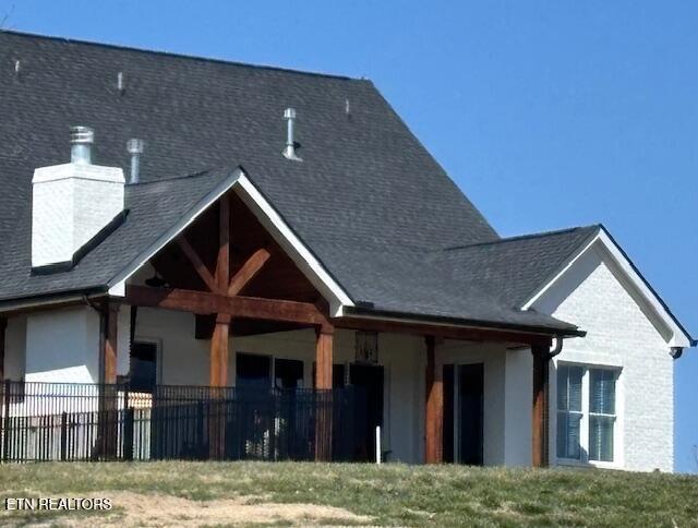 rear view of house featuring fence, roof with shingles, and a chimney