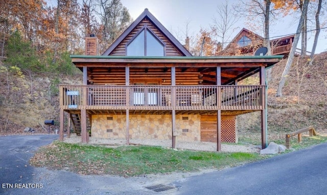 view of front of house featuring a wooden deck, stone siding, a chimney, and stairs