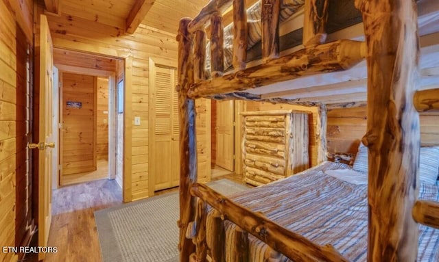 bedroom with wooden walls, beamed ceiling, wooden ceiling, and wood finished floors