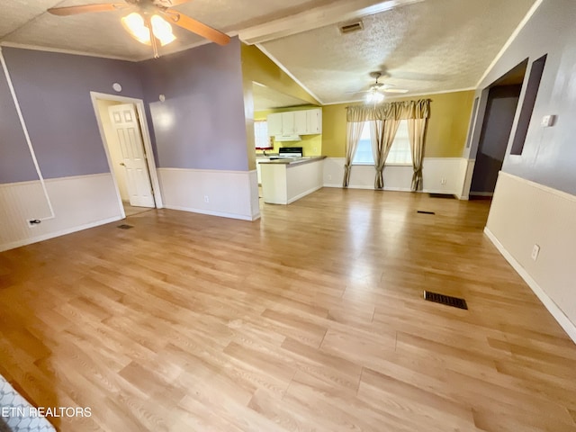 unfurnished living room featuring visible vents, a wainscoted wall, light wood finished floors, and ceiling fan