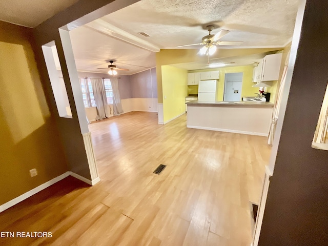 unfurnished living room featuring baseboards, visible vents, ceiling fan, a textured ceiling, and light wood-type flooring