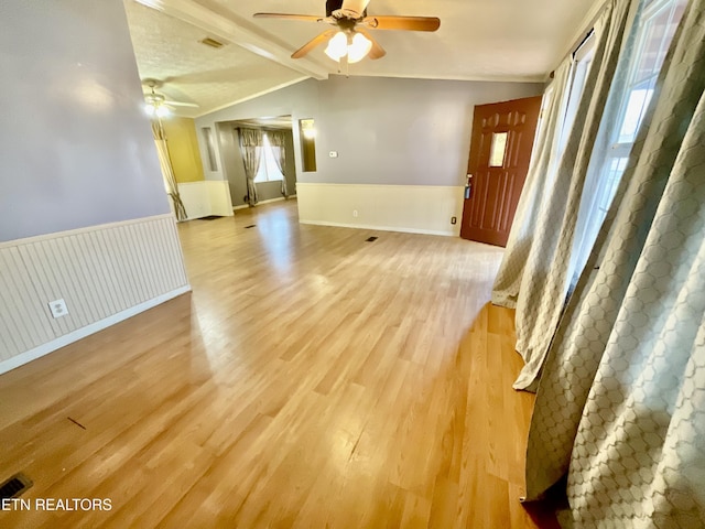 interior space with lofted ceiling with beams, light wood-style flooring, a ceiling fan, and a wainscoted wall