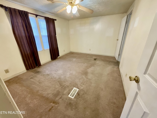 carpeted empty room featuring baseboards, visible vents, a textured ceiling, and ceiling fan