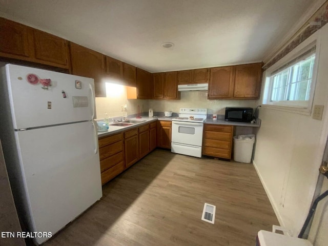 kitchen featuring visible vents, under cabinet range hood, a sink, white appliances, and light wood finished floors