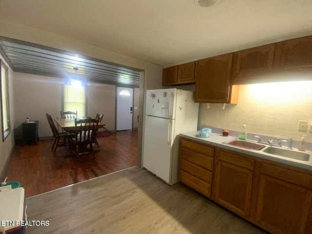 kitchen featuring light wood-type flooring, a sink, backsplash, freestanding refrigerator, and brown cabinetry