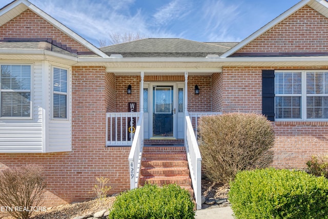 view of exterior entry with brick siding and a shingled roof