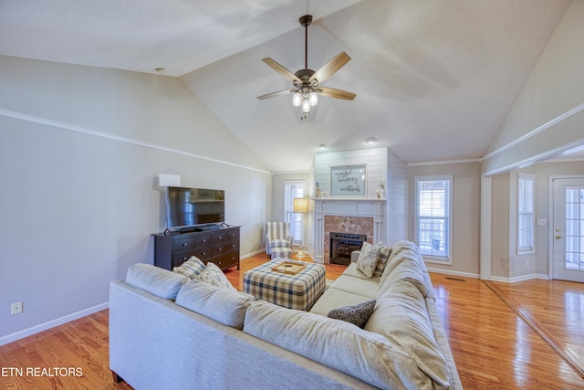 living area featuring a tiled fireplace, plenty of natural light, baseboards, and light wood-type flooring