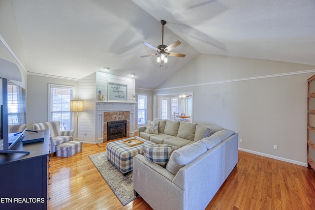 living room featuring light wood finished floors, ceiling fan, baseboards, lofted ceiling, and a tile fireplace