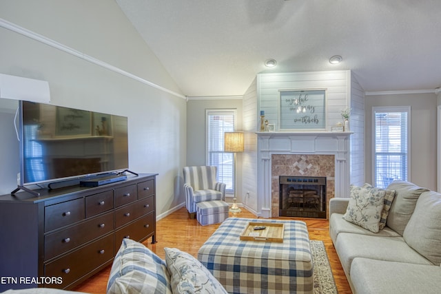 living area featuring a tiled fireplace, lofted ceiling, plenty of natural light, and light wood-style floors