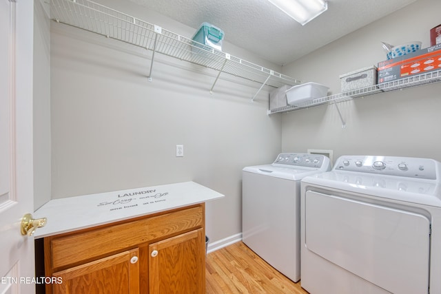 laundry room with cabinet space, a textured ceiling, light wood-style floors, and separate washer and dryer