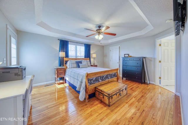 bedroom featuring a raised ceiling, light wood finished floors, and a textured ceiling