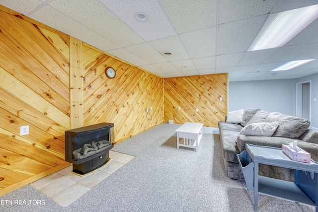 living area with a drop ceiling, carpet flooring, wood walls, and a wood stove