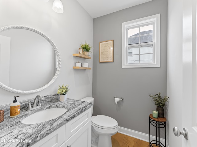 half bath with baseboards, toilet, wood finished floors, and vanity