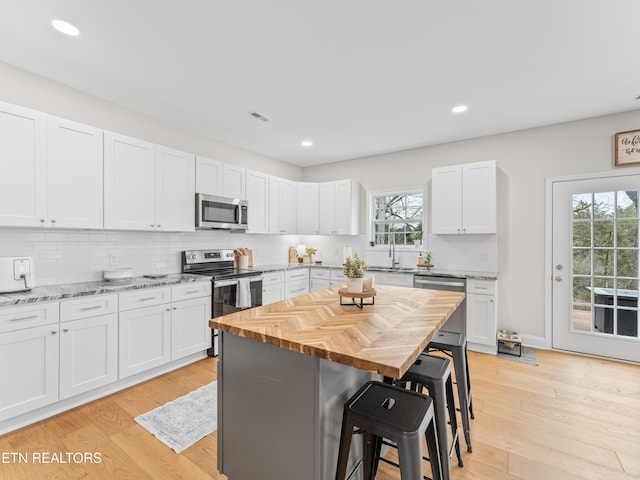 kitchen with a kitchen bar, decorative backsplash, light wood-style floors, and stainless steel appliances