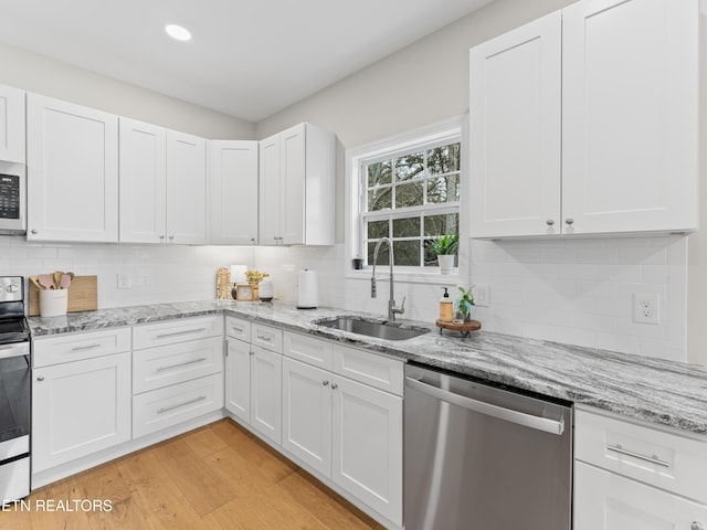 kitchen featuring light wood finished floors, tasteful backsplash, appliances with stainless steel finishes, white cabinets, and a sink