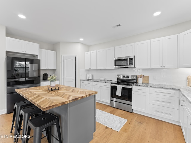 kitchen featuring light wood-style flooring, a breakfast bar area, wooden counters, and stainless steel appliances