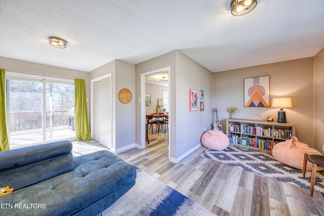 living area with baseboards, a textured ceiling, and wood finished floors