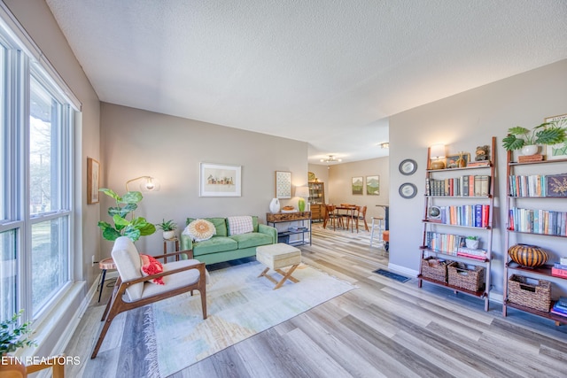 living area featuring light wood-type flooring, baseboards, and a textured ceiling