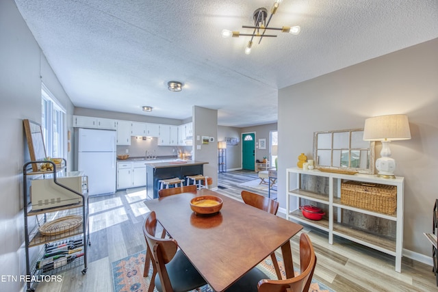 dining space with baseboards, an inviting chandelier, a textured ceiling, and light wood-style floors