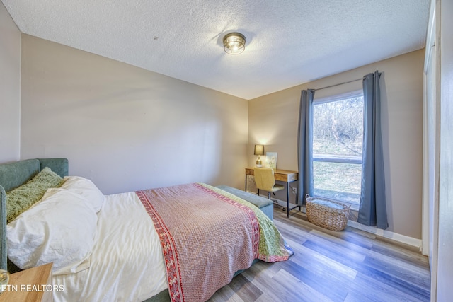 bedroom with baseboards, a textured ceiling, and wood finished floors