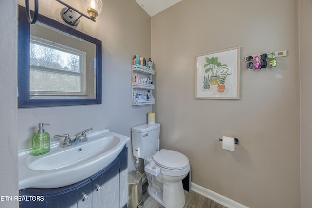 half bath with vanity, toilet, wood finished floors, and baseboards