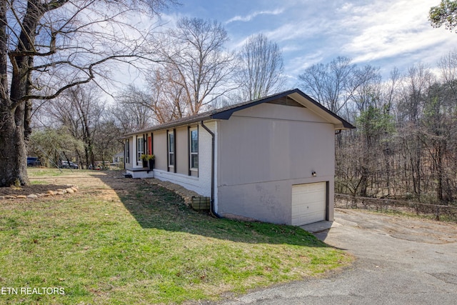 view of property exterior featuring brick siding, an attached garage, driveway, and a lawn