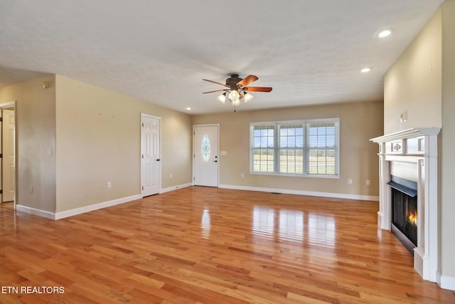 unfurnished living room featuring a ceiling fan, light wood-style floors, baseboards, and a warm lit fireplace