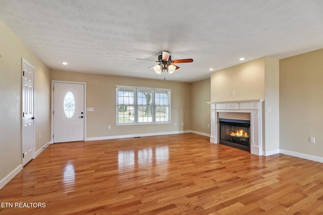 entryway featuring a ceiling fan, baseboards, light wood-style flooring, recessed lighting, and a glass covered fireplace