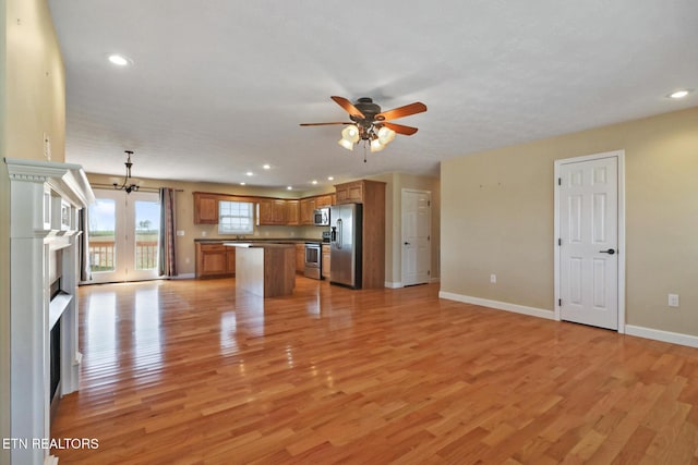 unfurnished living room with baseboards, light wood-style flooring, a fireplace, and ceiling fan with notable chandelier