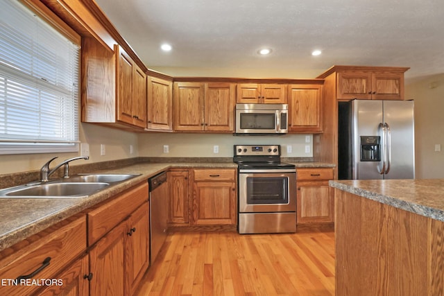 kitchen with light wood-type flooring, brown cabinets, appliances with stainless steel finishes, and a sink