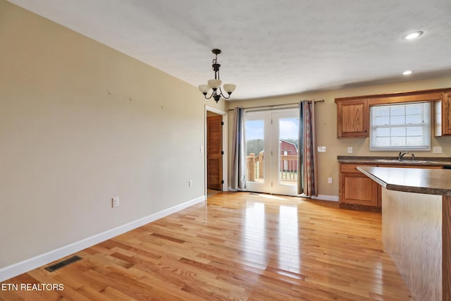 kitchen with visible vents, baseboards, light wood-type flooring, brown cabinetry, and a notable chandelier