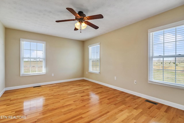 empty room with a ceiling fan, light wood-style floors, visible vents, and baseboards