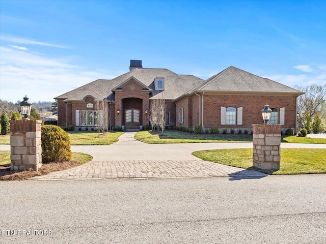 view of front of house with brick siding, curved driveway, a shingled roof, a front yard, and a chimney