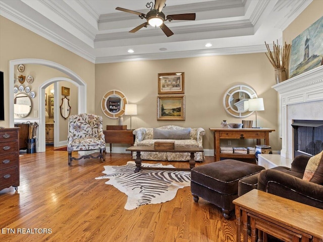 living area with crown molding, ceiling fan, wood finished floors, arched walkways, and a raised ceiling