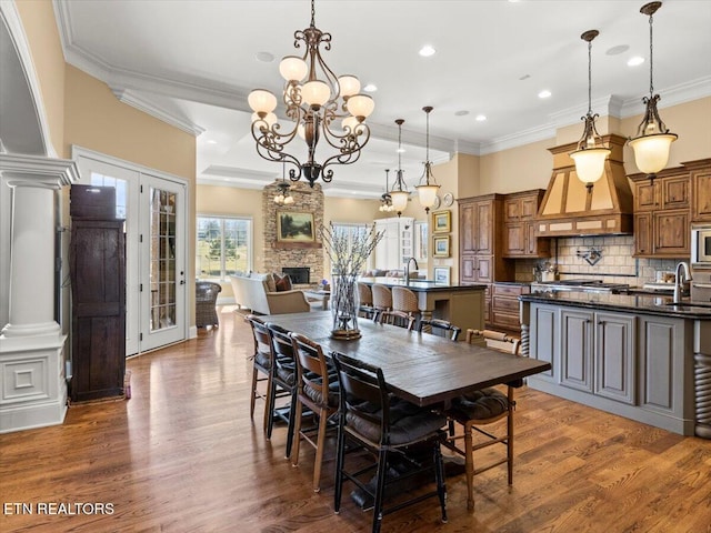 dining room featuring dark wood-style floors, a chandelier, a stone fireplace, and ornamental molding