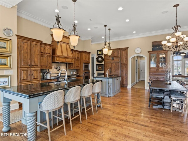 kitchen featuring a spacious island, arched walkways, a sink, stainless steel appliances, and light wood-style floors