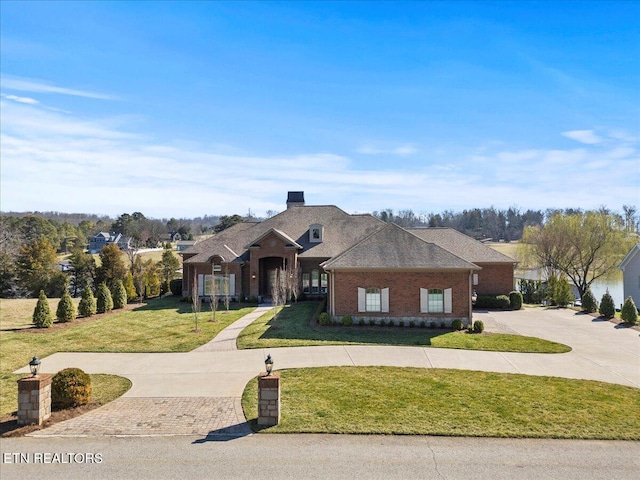 view of front of house with brick siding, curved driveway, a shingled roof, and a front lawn