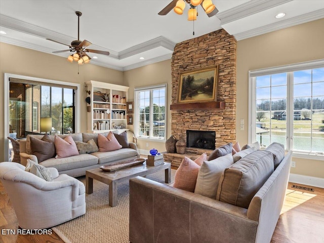 living room with a stone fireplace, wood finished floors, a ceiling fan, and visible vents