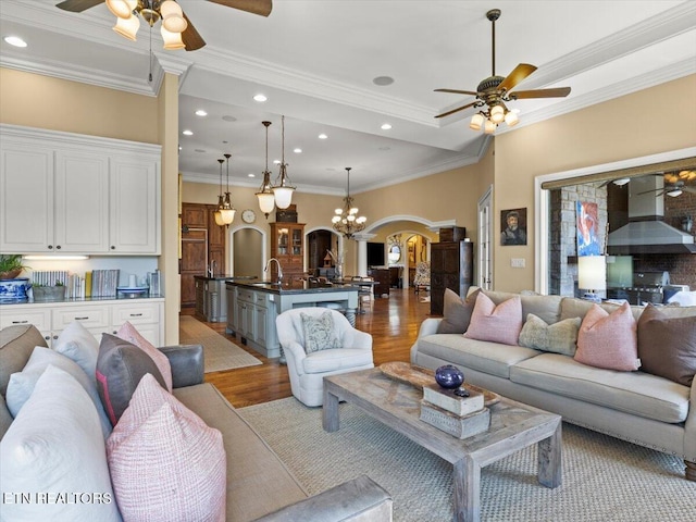 living area featuring light wood finished floors, ornamental molding, recessed lighting, ceiling fan with notable chandelier, and arched walkways