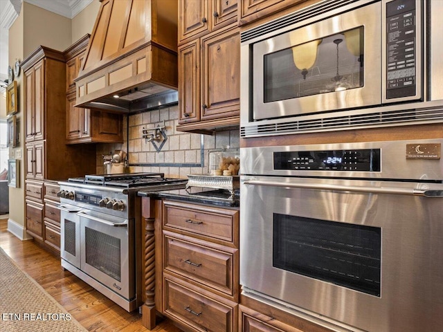 kitchen with light wood finished floors, backsplash, crown molding, custom exhaust hood, and stainless steel appliances