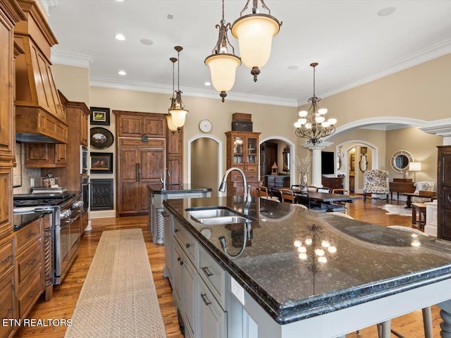 kitchen featuring wood finished floors, double oven range, arched walkways, a large island with sink, and a sink