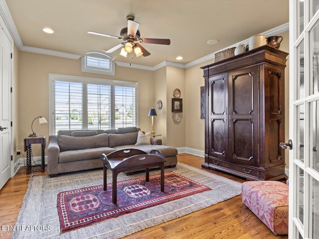 living room featuring baseboards, light wood-type flooring, crown molding, and ceiling fan