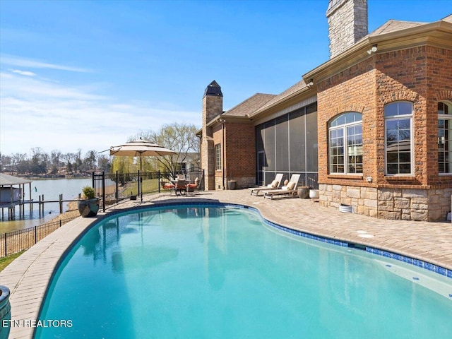 view of pool with a fenced in pool, a water view, fence, a sunroom, and a patio area