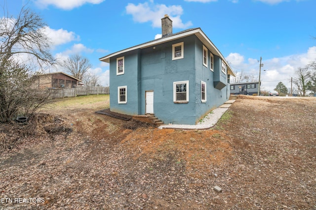 rear view of house featuring stucco siding, fence, and a chimney