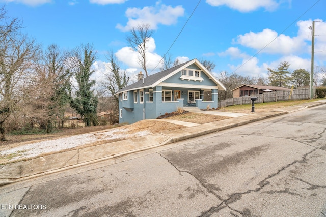 view of front of home featuring stucco siding, fence, covered porch, and a chimney